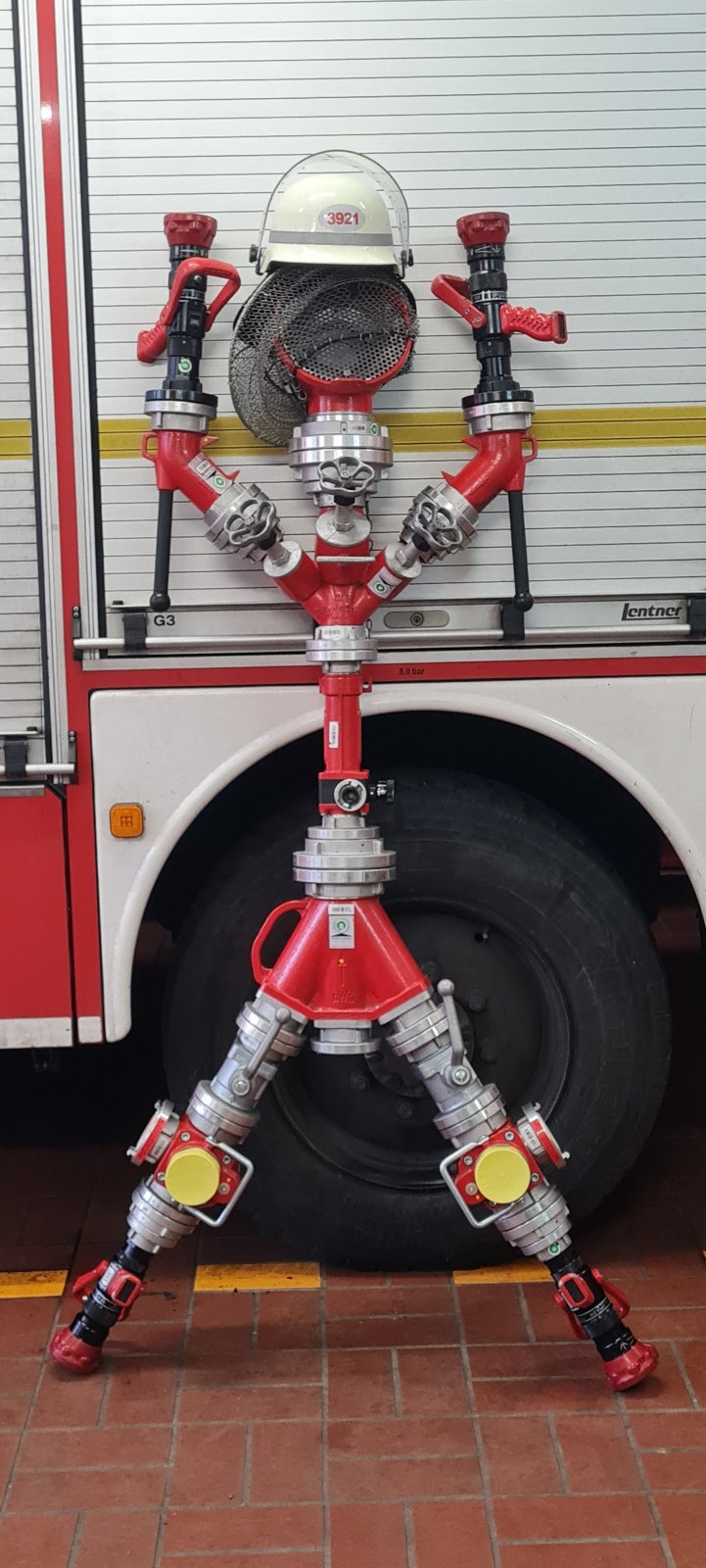 Eine Figur aus Strahlrohren und Kupplungen vor dem Löschfahrzeug